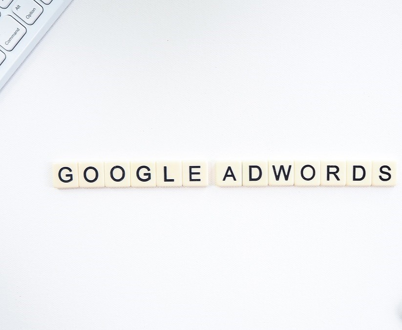 Scrabble-Steine liegen auf einem weißen Bürotisch und bilden die Phrase "Google Adwords"